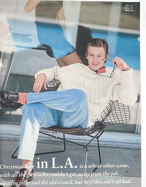 man sitting in chair with white cable knit sweater, jeans, red socks and loafers. christmas here in la is a whole other scene...