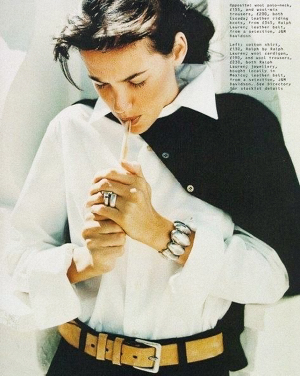 woman in white button up, smoking a cigarette, brown belt with jewlery and black cardigan